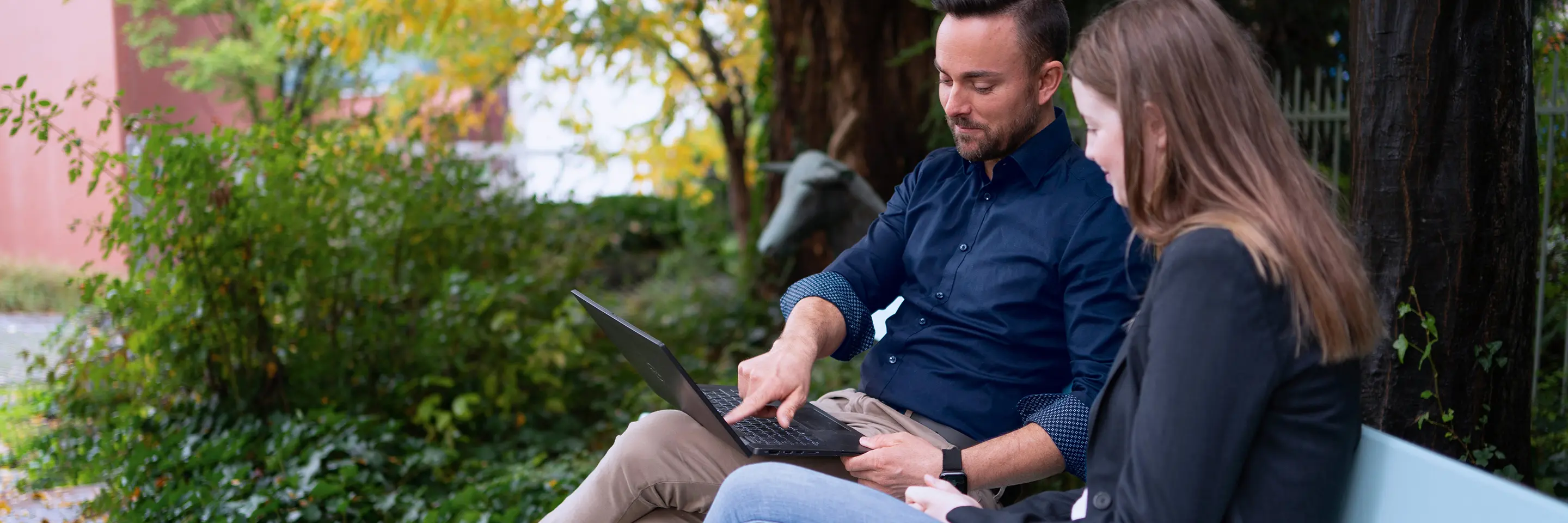 Two people sit outside on a bench and look at a laptop together