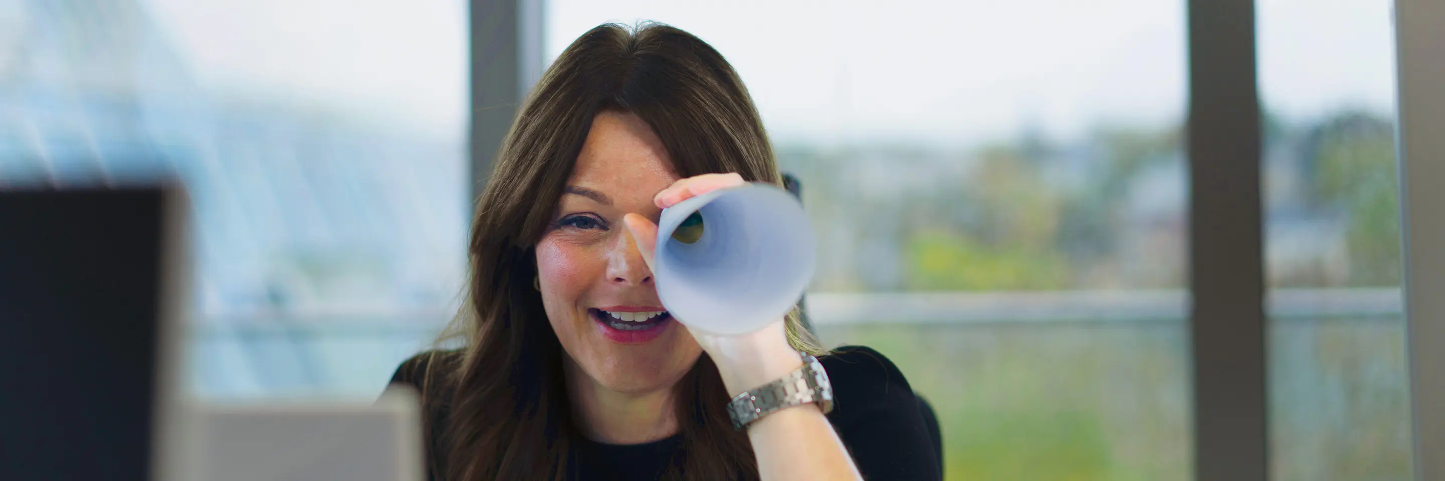 A woman looks towards us through a rolled-up piece of paper