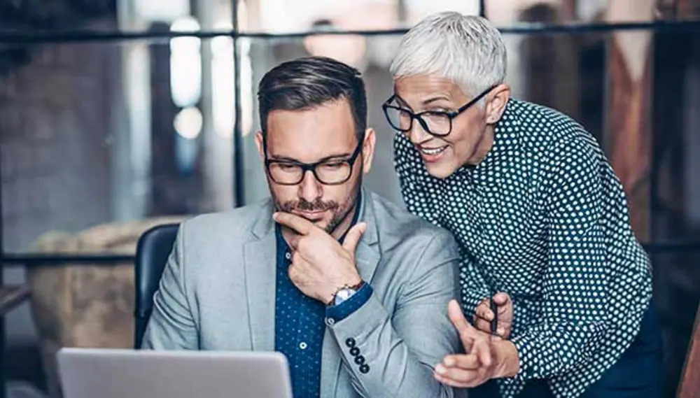 A man and a woman talk in front of a laptop.