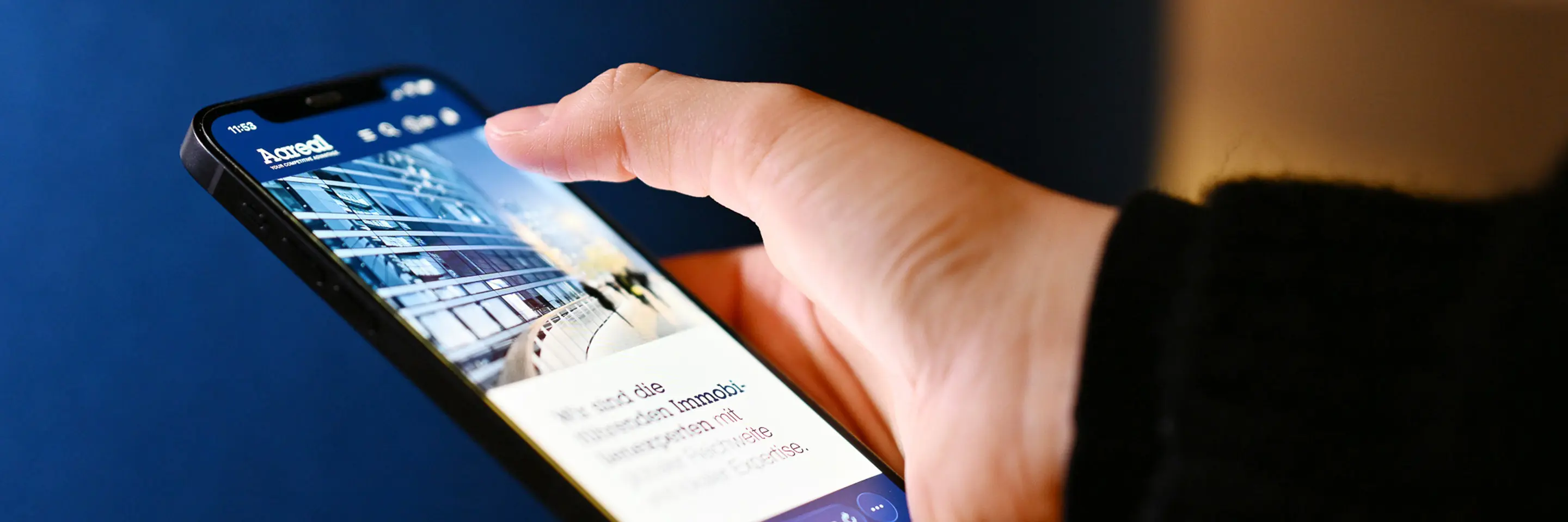 Hand hält ein Smartphone und scrollt auf der Website der Aareal Bank mit Abbildung eines modernen Gebäudes.