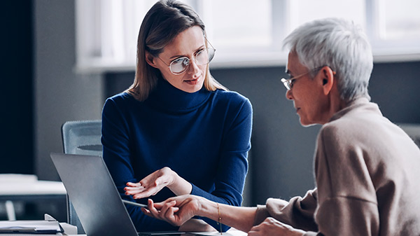 Two women talk in front of a laptop