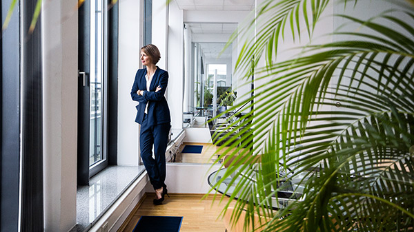 A woman stands by a window and looks out.